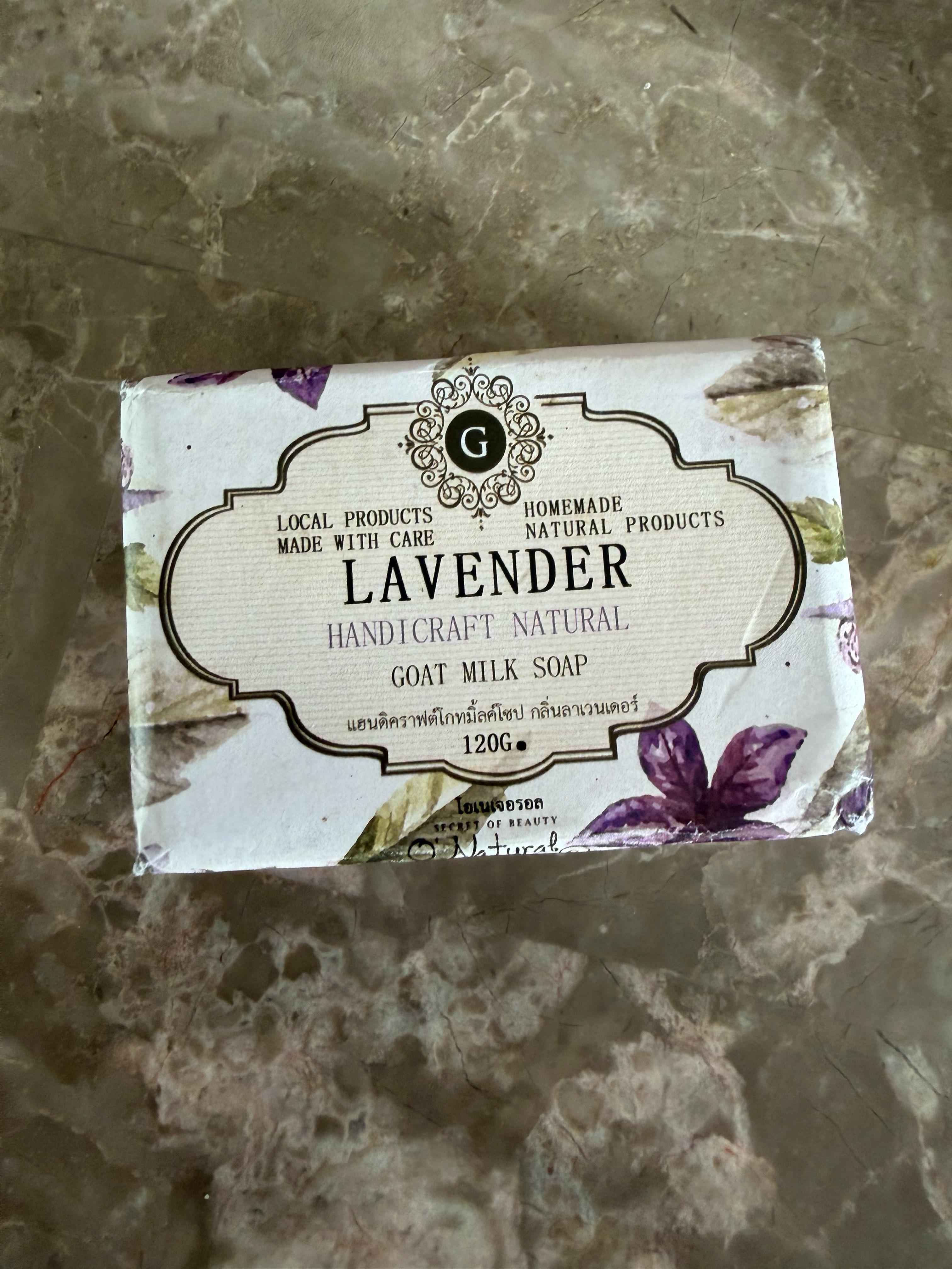 Lavender goat milk soap bar with packaging on a textured surface